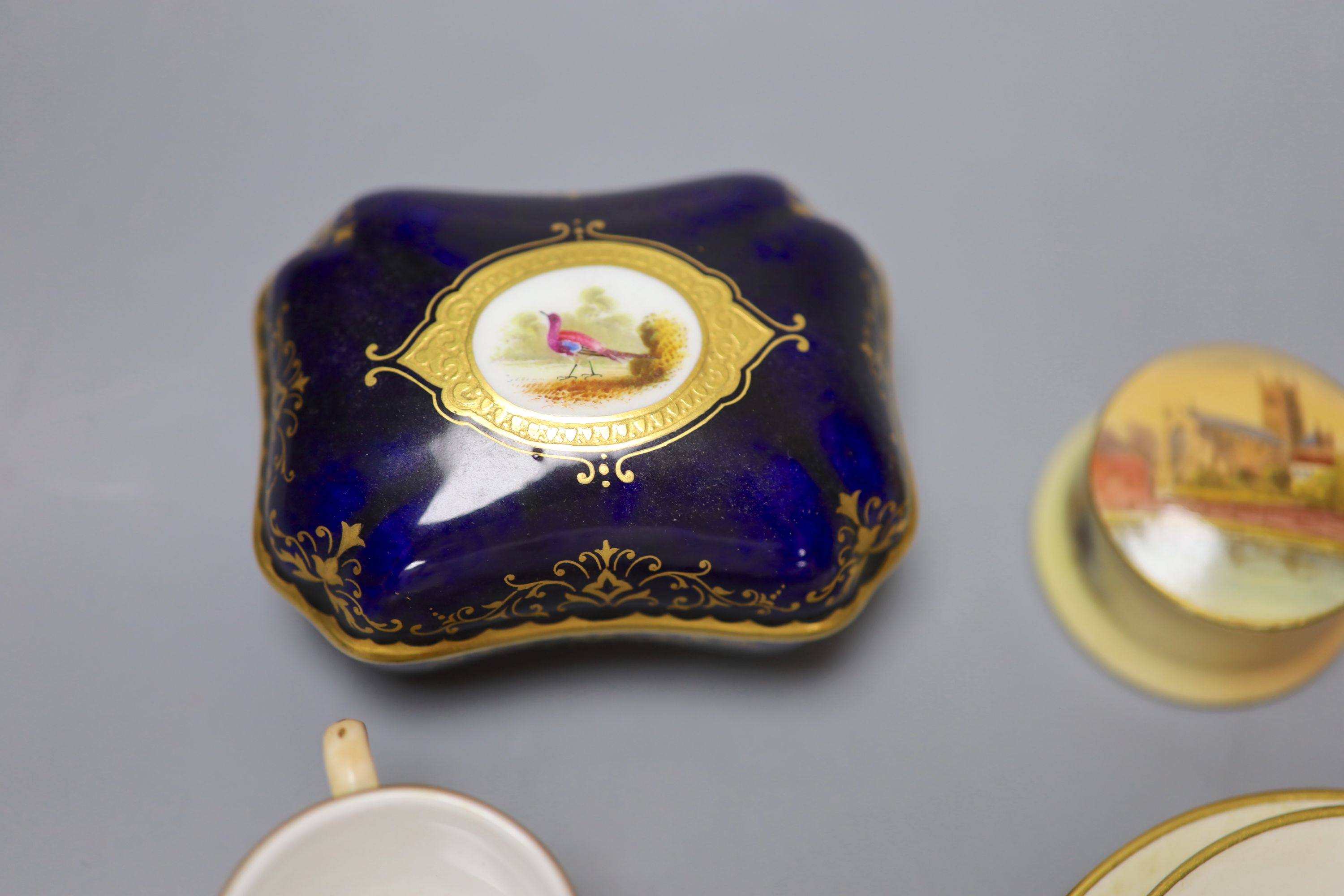 An early 20th century Coalport box and cover painted with a bird on a blue ground, a Coalport miniature gilt ground mug with landscape,